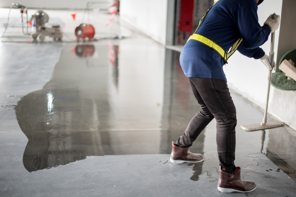 Construction worker painting epoxy flooring or floor hardener